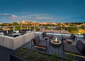 Thumbnail 28 of 30 - A rooftop patio with a fire pit and seating area overlooking a city skyline.