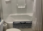 Thumbnail 15 of 15 - A white bathroom with a toilet, a shower with a white curtain, and a black and white towel.