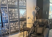 Thumbnail 9 of 15 - A black leather massage chair sits in front of a wall of framed photos.