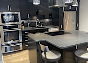 Thumbnail 4 of 15 - A modern kitchen with a large island and stainless steel appliances.