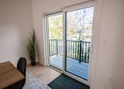 Thumbnail 13 of 44 - A room with a table and a chair is shown with a view of a deck outside through a sliding glass door.