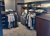 Thumbnail 1 of 15 - A walk in closet with clothes hanging and shelves.
