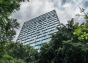 Thumbnail 1 of 31 - a tall building with trees in the foreground and a cloudy sky