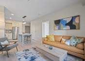 Thumbnail 53 of 59 - a living room with a brown couch and a coffee table in front of a kitchen with a