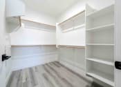 Thumbnail 26 of 49 - a walk in closet with white walls and wooden floors