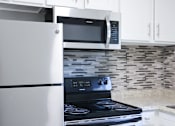 Thumbnail 18 of 30 - A modern kitchen with a stainless steel refrigerator, microwave, and stove.