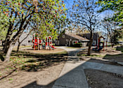 Thumbnail 14 of 18 - A playground with a red slide and a green tree.