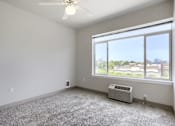 Thumbnail 20 of 32 - A room with a ceiling fan, carpeted floor, and a window overlooking a cityscape.