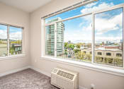 Thumbnail 22 of 32 - A room with a window showing a view of a cityscape and a wall-mounted air conditioner.