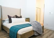 Thumbnail 27 of 31 - A bed with a white sheet and a blue blanket is in the foreground of a room with a wooden headboard at Zora Encanto, Arizona