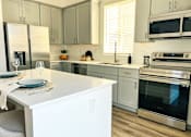 Thumbnail 24 of 31 - A modern kitchen with a white island and stainless steel appliances at Zora Encanto, Phoenix, AZ