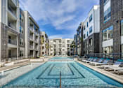 Thumbnail 17 of 40 - A long rectangular pool in the middle of a courtyard surrounded by buildings at Arise Riverside Apartments, Texas 78741