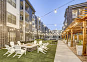 Thumbnail 14 of 40 - A patio with white chairs and a table is surrounded by apartment buildings at Arise Riverside Apartments, Austin, TX, 78741