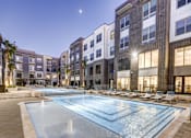 Thumbnail 16 of 40 - A large swimming pool in front of apartment buildings at dusk at Arise Riverside Apartments, Austin, TX