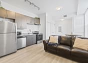Thumbnail 6 of 24 - a living room with a leather couch and a kitchen with stainless steel appliances