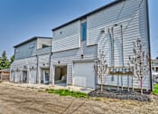 Thumbnail 8 of 73 - A large grey building with a garage door open and a tree in front.