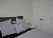 Thumbnail 5 of 9 - A bed with white pillows and a cat bed with a cat in it at The Laurent at Laurel Apartments, Edmonton