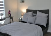Thumbnail 9 of 9 - A bed with a white comforter and a black headboard with a picture of a flower on the wall at The Laurent at Laurel Apartments, Edmonton, AB