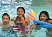 Thumbnail 8 of 10 - Three girls are in a pool with pool noodles.