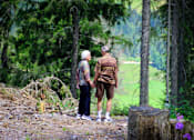 Thumbnail 2 of 11 - Two people are standing on a dirt path in the woods.