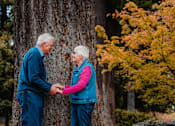 Thumbnail 4 of 11 - An elderly couple holding hands in front of a tree.