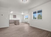 Thumbnail 6 of 13 - A spacious room with wooden flooring and a kitchen area in the background.