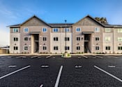 Thumbnail 1 of 13 - A large building with a parking lot in front of it.