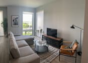 Thumbnail 8 of 16 - A living room with a brown sofa, a coffee table, a television, and a rug.