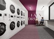 Thumbnail 23 of 30 - A person is sitting on a chair in front of a row of washing machines.