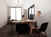 Thumbnail 27 of 30 - A man is sitting at a table with a laptop and a plant in the room.