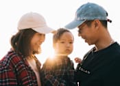 Thumbnail 2 of 10 - A family of three wearing hats and casual clothing are standing together.