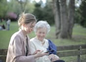 Thumbnail 6 of 11 - A young woman and an older woman are sitting on a bench in a park.