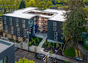 Thumbnail 39 of 41 - A modern building with a green logo on the side is surrounded by trees and has a parking lot in front.