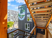 Thumbnail 23 of 41 - A wooden staircase leads to a balcony with a mural of a bear on the side of a building.
