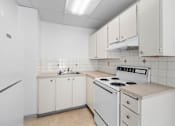 Thumbnail 24 of 35 - A white kitchen with a stove top oven and a sink.