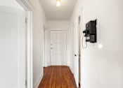 Thumbnail 23 of 35 - A hallway with a door on the left and a wall-mounted TV on the right.