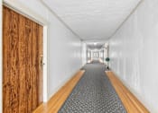 Thumbnail 25 of 35 - A long hallway with a wooden door on the left and a carpeted floor.