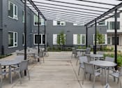 Thumbnail 4 of 38 - A patio with tables and chairs is surrounded by apartment buildings.