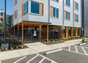 Thumbnail 24 of 38 - A modern building with a grey and orange facade is surrounded by a parking lot.