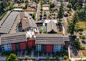 Thumbnail 1 of 21 - A modern building with a red and white facade is surrounded by trees and other buildings.
