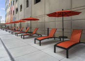 Thumbnail 38 of 76 - a row of orange lounge chairs with red umbrellas in front of a building at The Icon, Richmond, VA 23230