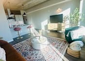 Thumbnail 1 of 18 - A living room with a rug, a couch, a television, and a kitchen area in the background.