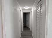 Thumbnail 21 of 25 - A long, narrow hallway with white walls and a wooden floor.