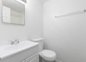Thumbnail 6 of 24 - A white bathroom with a toilet, sink, mirror, and towel bar.