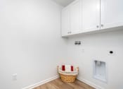 Thumbnail 17 of 38 - A laundry basket with a red and white striped cover sits on a wooden floor in a room with white walls and cabinets.