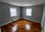 Thumbnail 6 of 7 - A room with wooden floors and two windows.