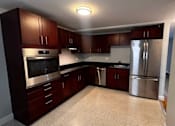 Thumbnail 5 of 7 - A kitchen with dark wood cabinets and stainless steel appliances.
