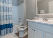 Thumbnail 8 of 35 - A white toilet in a bathroom with a blue and white shower curtain.