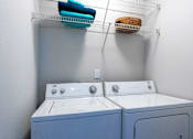 Thumbnail 11 of 35 - Two washing machines are in a laundry room with towels hanging above them.
