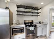 Thumbnail 13 of 42 - A modern kitchen with a stainless steel refrigerator, microwave, oven, and shelves above the counter.
